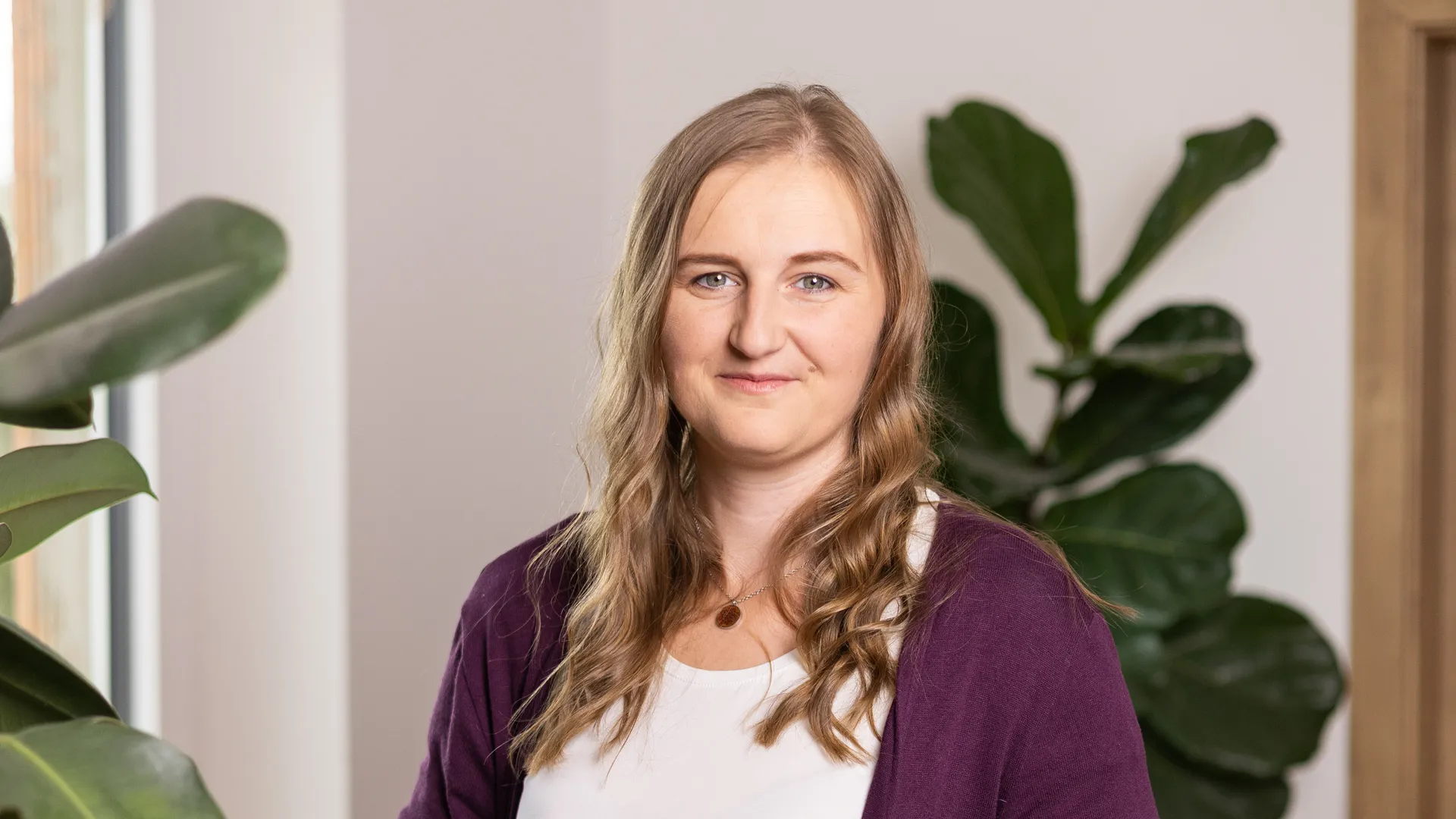 Stephanie Rosenmayer in ihrem hellen Praxisraum, umgeben von Pflanzen, mit ruhigem und professionellem Blick in die Kamera.